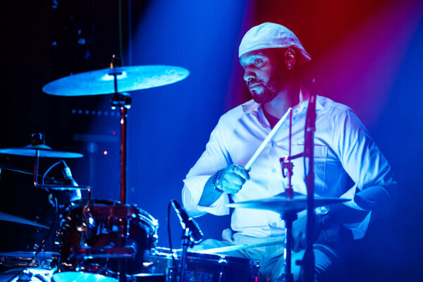 A man in a white hat playing drums on stage.