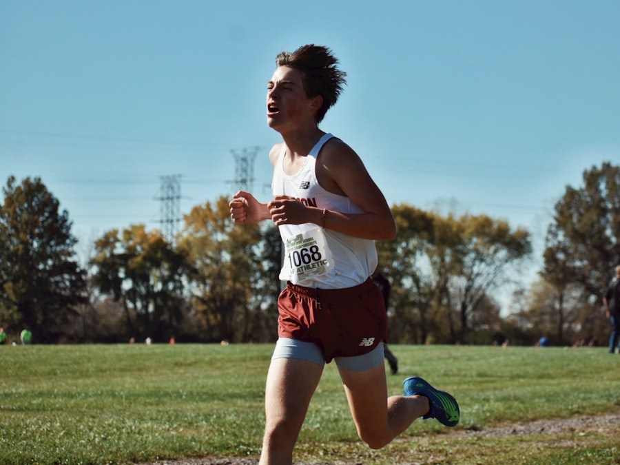 A male cross country runner racing across a grassy field.
